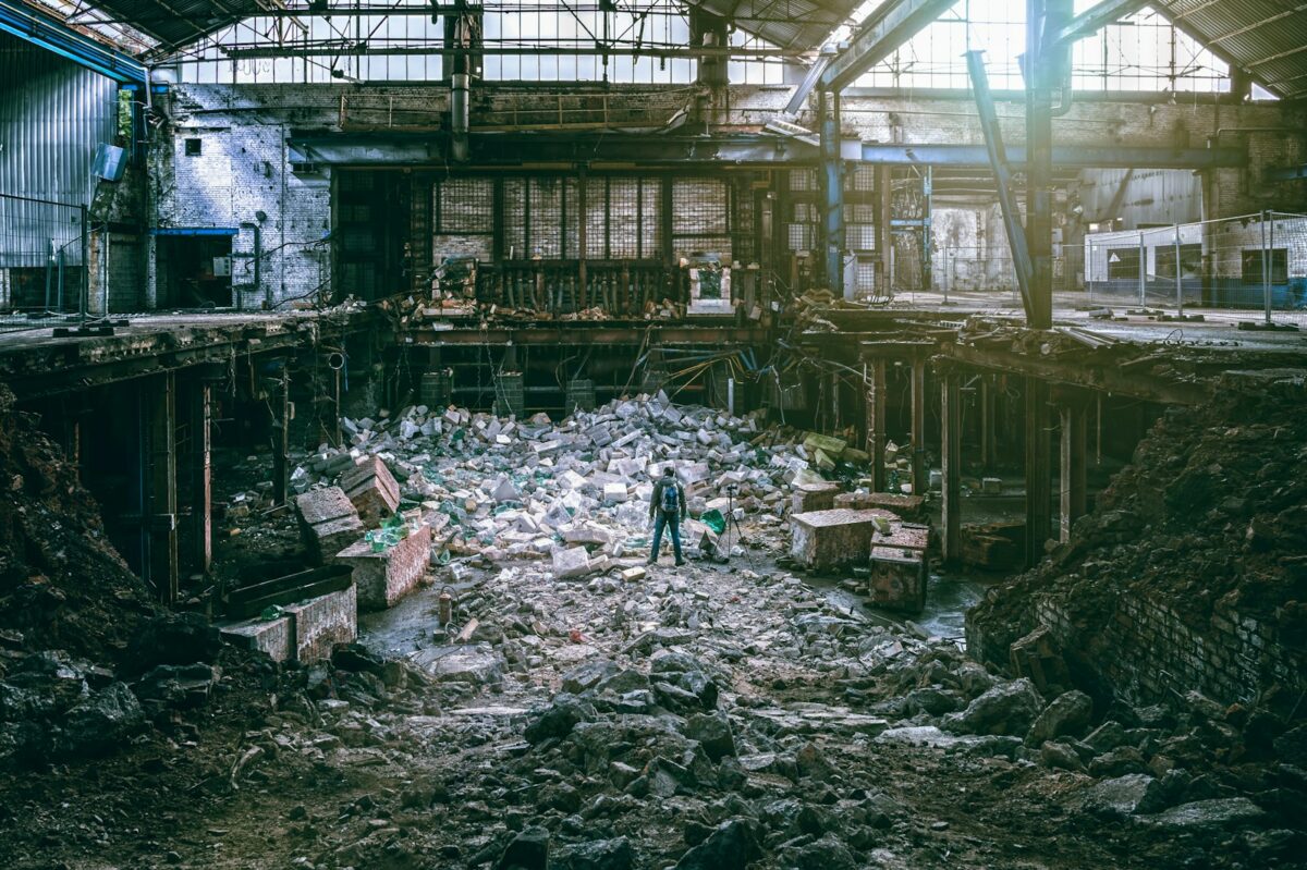 A person standing in the middle of the rubble of what looks an empty factory